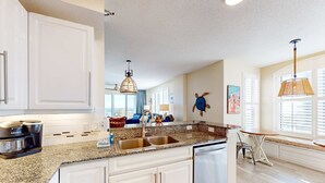 Una cocina moderna con encimeras de granito, armarios blancos, lavavajillas integrado y cafetera.