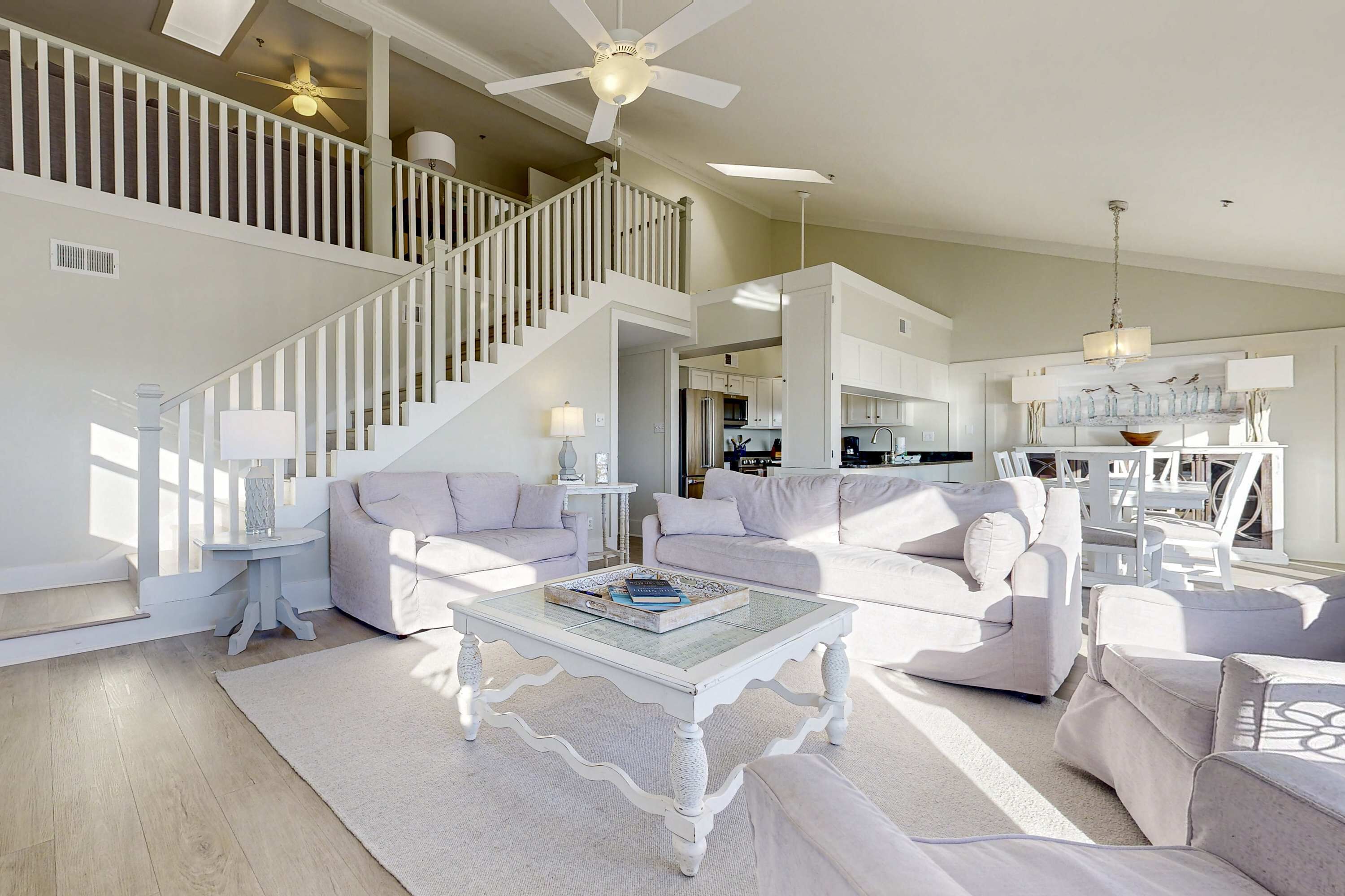 Ein geräumiges Wohnzimmer mit hohen Decken, einer Treppe und einer Küche im Hintergrund.