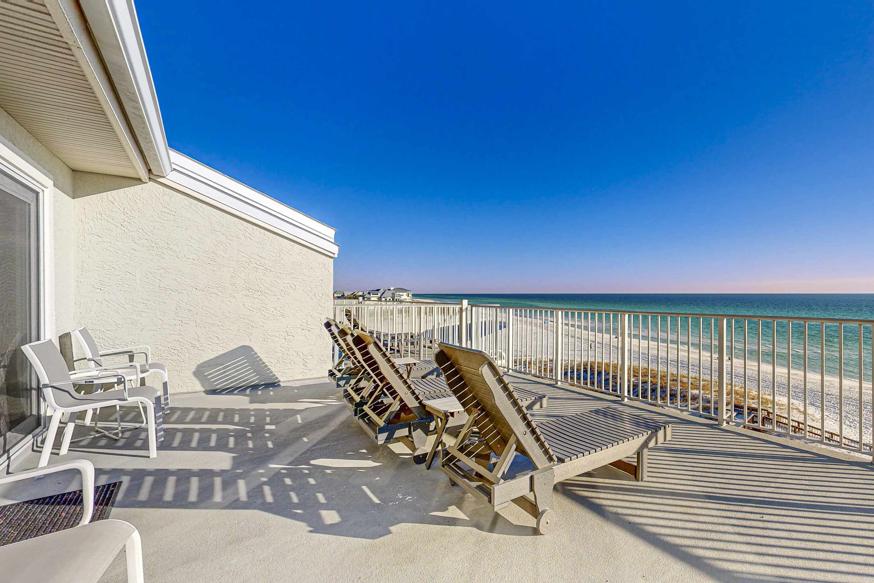 A balcony with beach chairs and a table, overlooking a sandy beach and the ocean.