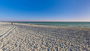 Een breed zandstrand met voetafdrukken die naar het water leiden, een heldere lucht en een rustige zee.