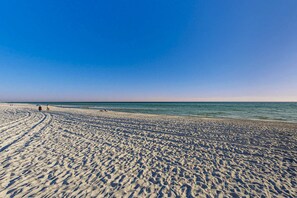 A wide sandy beach with footprints leading to the water, a clear sky, and a calm sea. - Fourth floor oceanfront condo with pool access, ocean views, and washer&dryer (Santa Rosa Beach)