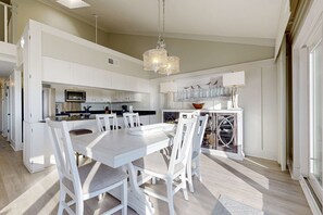 Een moderne keuken met witte kasten, een eethoek met een witte tafel en stoelen, en een kroonluchter.