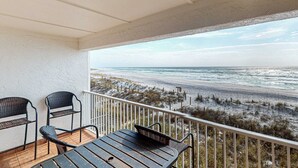 Ein Balkon mit einem Holztisch und zwei Stühlen, der Blick auf einen Strand mit Dünen und dem Meer geht.