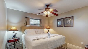 Ein ordentlich bezogenes Bett mit Handtuch, Deckenventilator, zwei Nachttischlampen und gerahmten Bildern an der Wand.