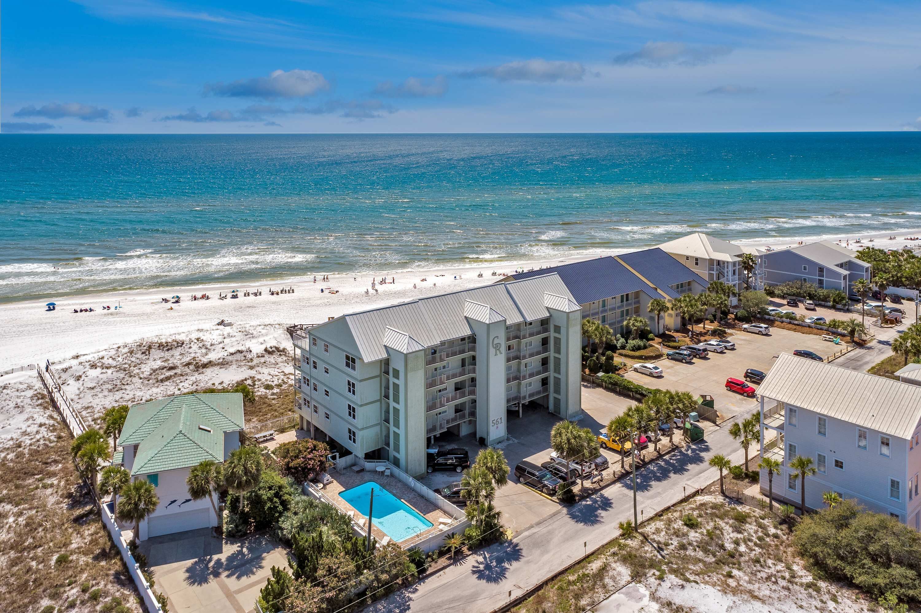 A beachfront hotel with multiple buildings, a swimming pool, and a beach in the background.