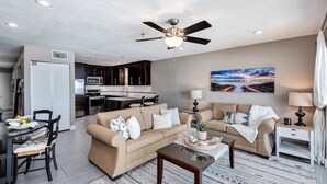 A living room with a beige sofa, a coffee table, and a dining area with a table and chairs. - Stylish oceanfront condo w/ pool access, private W/D, ocean views, & central AC (Santa Rosa Beach)
