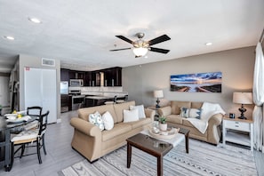 A living room with a beige sofa, a coffee table, and a dining area with a table and chairs. - Stylish oceanfront condo w/ pool access, private W/D, ocean views, & central AC (Santa Rosa Beach)