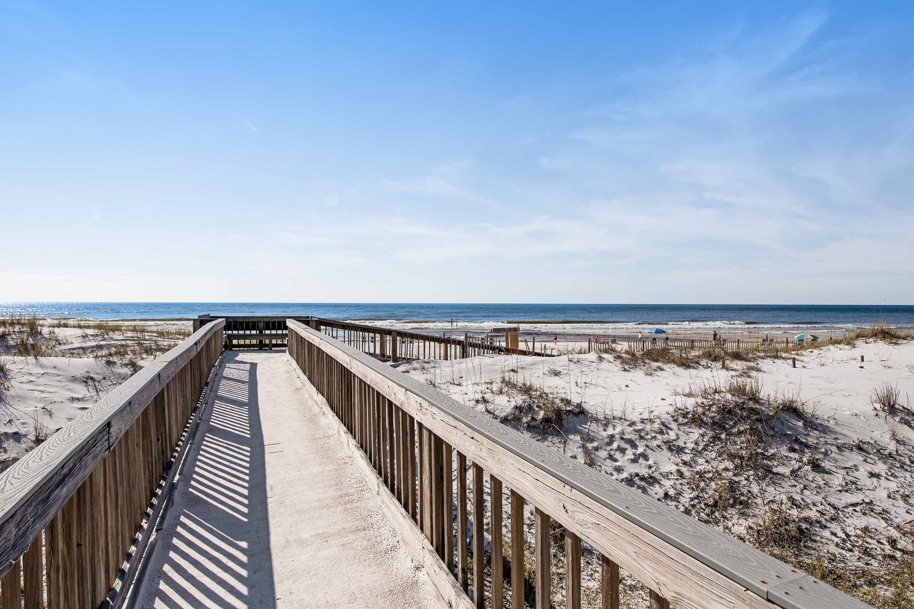 A wooden boardwalk leading to a beach with sand dunes and the ocean in the background.