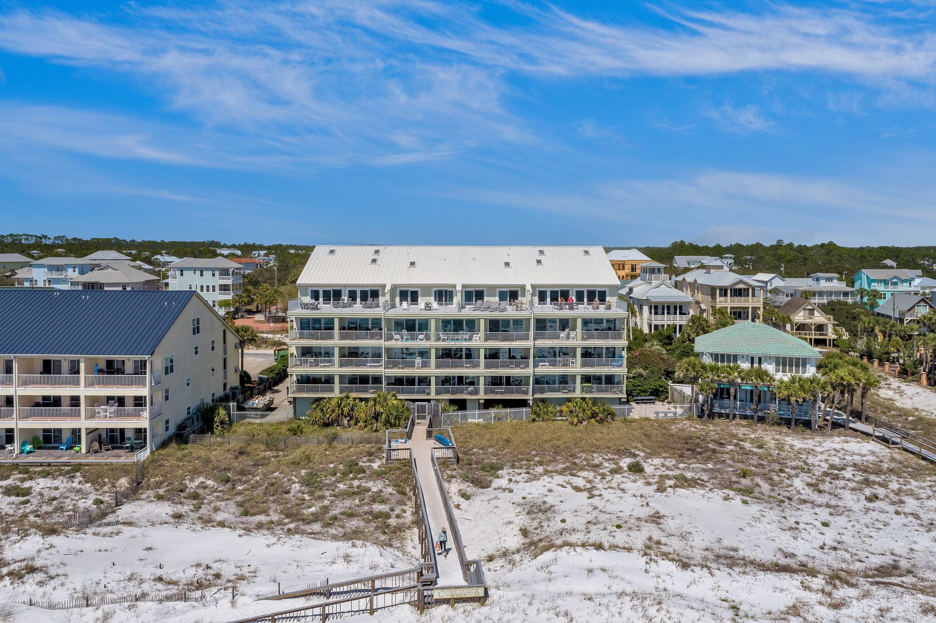 Un hotel frente a la playa con varios pisos, un paseo marítimo que conduce a la orilla y vistas al océano.