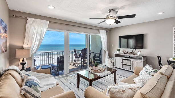 A spacious living room with a large TV, a ceiling fan, and a balcony with a view of the beach. - Stylish oceanfront condo w/ pool access, private W/D, ocean views, & central AC (Santa Rosa Beach)