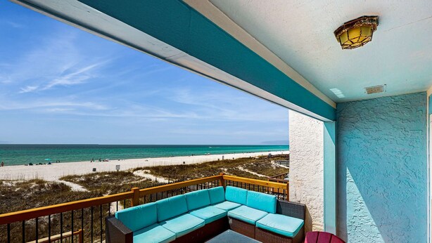 A balcony with a wicker sofa and a red chair, overlooking a beach with sand and dunes. - Oceanfront Townhouse w/ Ocean Views, High-Speed WiFi, Washer/Dryer, & Central AC (Panama City Beach)