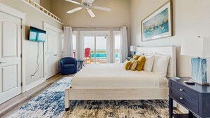 A bedroom with a bed, a ceiling fan, a TV, a nightstand, and a painting on the wall. - Oceanfront Townhouse w/ Ocean Views, High-Speed WiFi, Washer/Dryer, & Central AC (Panama City Beach)