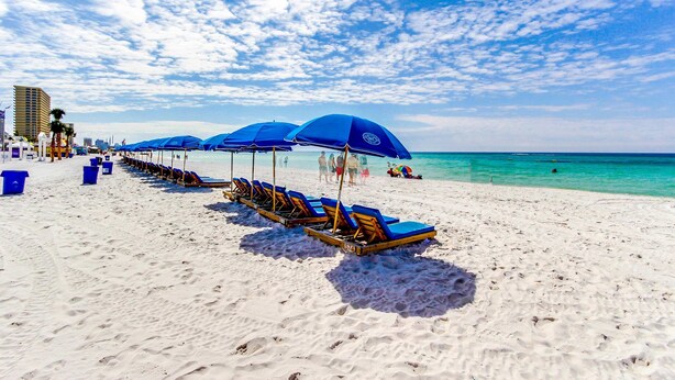 A beach with rows of blue umbrellas and lounge chairs, a sandy shore, and a clear blue sky. - 3rd-floor beachfront condo with Gulf views, outdoor pool, balconies, W/D, & AC (Panama City Beach)