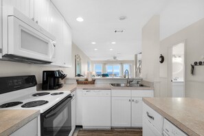A modern kitchen with white cabinetry, a stove, a dishwasher, and a coffee maker. - 3rd-floor beachfront condo with Gulf views, outdoor pool, balconies, W/D, & AC (Panama City Beach)