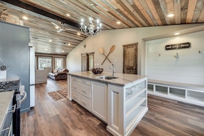 A modern kitchen with a central island, wooden ceiling, and a chandelier.