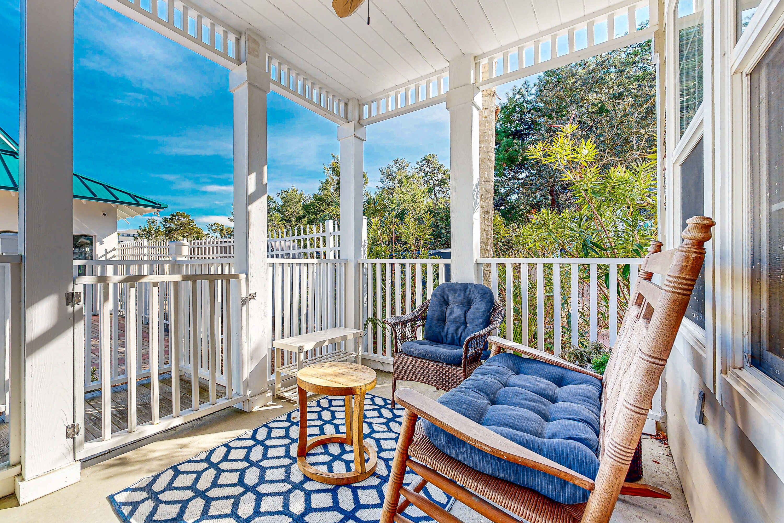 A covered outdoor area with a white railing, a wicker chair, a blue sofa, and a patterned rug.