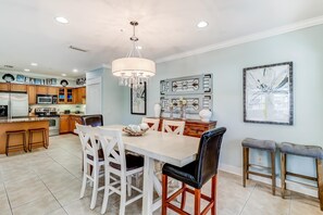A spacious kitchen with wooden cabinets, a white dining table, and a chandelier. - Coastal chic condo steps from the sand, shared pool & central location (Santa Rosa Beach)