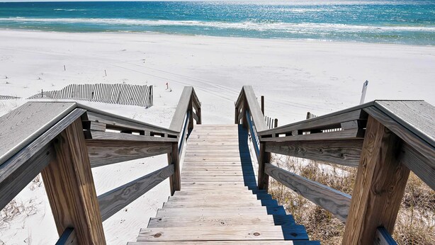 Un escalier en bois mène à une plage d’où l’on a une vue dégagée sur l’océan.