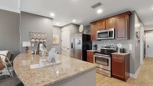 A modern kitchen with granite countertops, stainless steel appliances, and wooden cabinets. - 3rd-floor beach view condo with Pool, Hot tub, & private balcony (Panama City Beach)