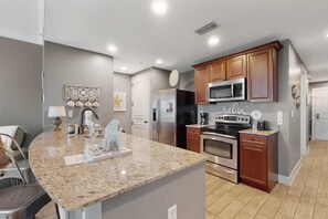 A modern kitchen with granite countertops, stainless steel appliances, and wooden cabinets. - 3rd-floor beach view condo with Pool, Hot tub, & private balcony (Panama City Beach)