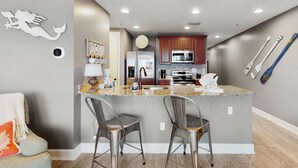 A modern kitchen with a central island, bar stools, and a refrigerator. - 3rd-floor beach view condo with Pool, Hot tub, & private balcony (Panama City Beach)