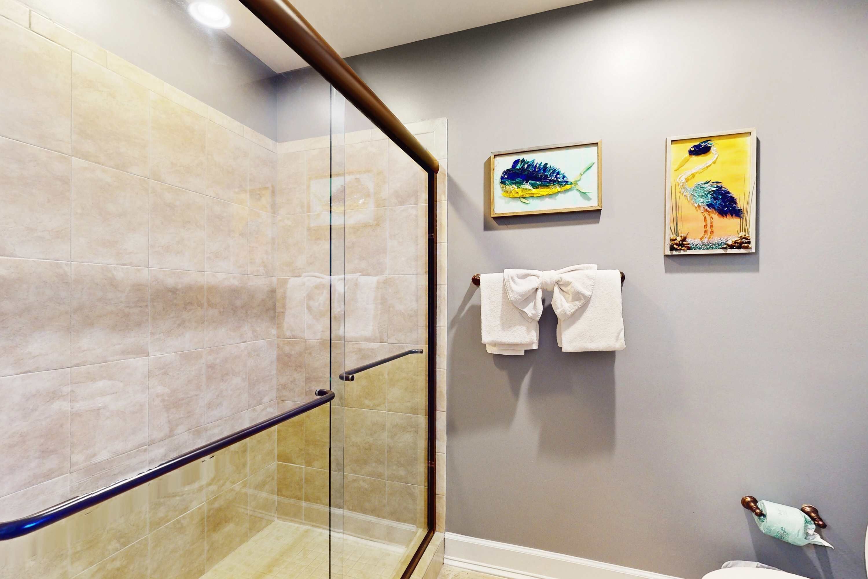 Un baño con cabina de ducha de vidrio, un perchero con dos toallas y dos cuadros en la pared.
