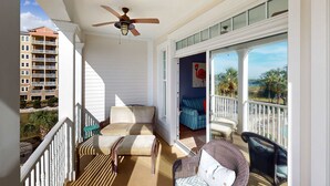 A balcony with a ceiling fan, wicker furniture, and a view of a building and palm trees. - 3rd-floor beach view condo with Pool, Hot tub, & private balcony (Panama City Beach)