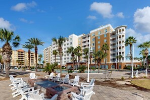 A resort with multiple-story buildings, outdoor seating areas with white chairs, and palm trees. - 3rd-floor beach view condo with Pool, Hot tub, & private balcony (Panama City Beach)