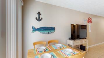 A dining area with a wooden table set for four, a television on a stand, and nautical-themed wall decorations.