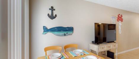 A dining area with a wooden table set for four, a television on a stand, and nautical-themed wall decorations.