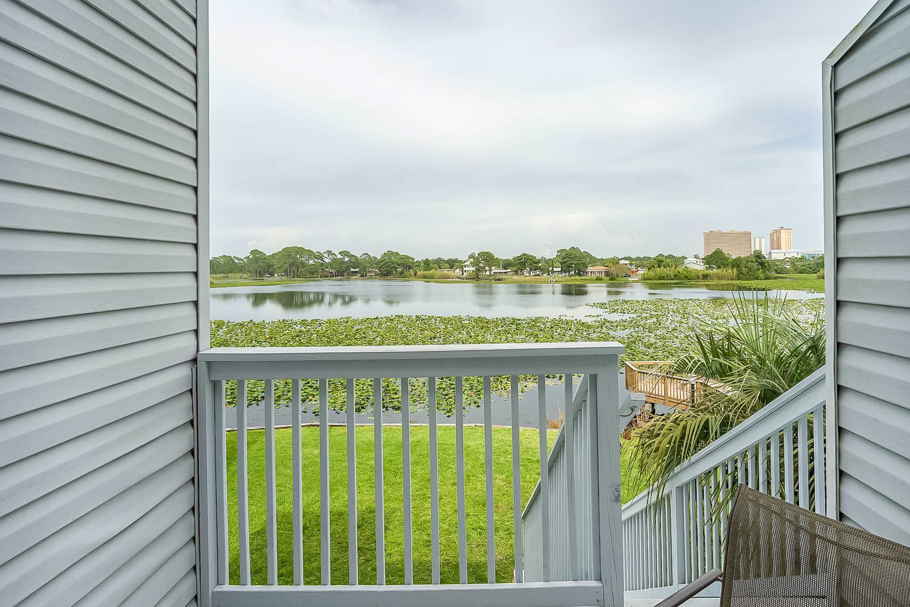A view from a balcony with a railing, overlooking a lake with lily pads and a grassy area.