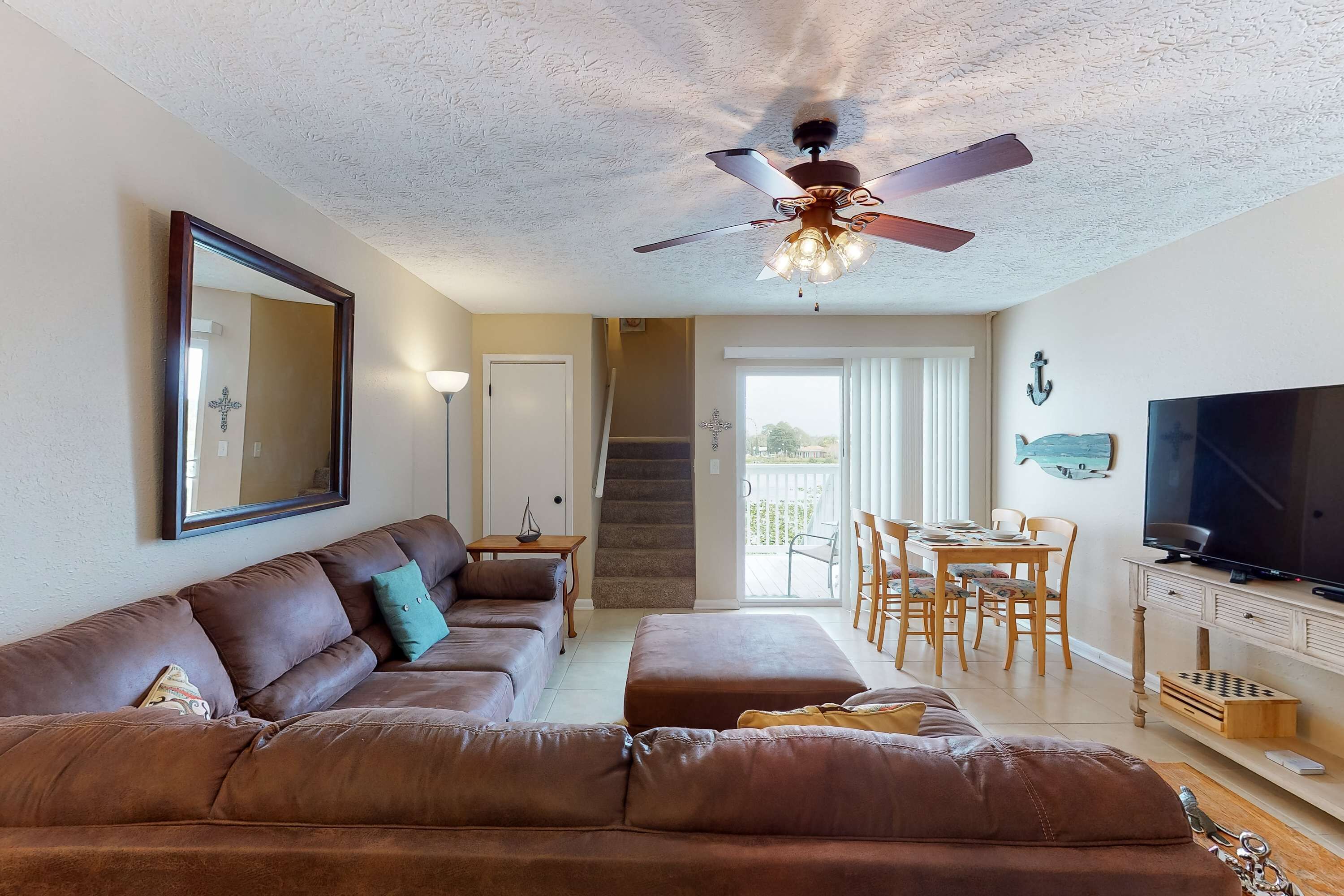 A living room with a brown leather sofa, a ceiling fan, a TV, and a dining area with wooden furniture.