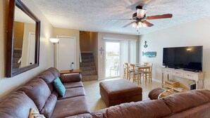 Un salon avec un canapé en cuir marron, un ventilateur de plafond, un téléviseur et un coin repas comprenant des chaises et une table.