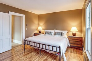 A bedroom with a bed, two bedside tables with lamps, a wooden floor, and a door. - Stay & Play in Ellicottville Village! Home w/ Deck (Ellicottville)