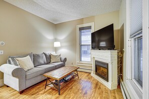 A living room with a gray sofa, wooden coffee table, fireplace, and a flat-screen TV. - Stay & Play in Ellicottville Village! Home w/ Deck (Ellicottville)