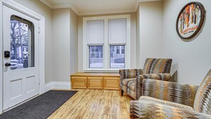 A room with a wooden floor, a bench, a patterned armchair, a door, and a window with blinds. - Stay & Play in Ellicottville Village! Home w/ Deck (Ellicottville)