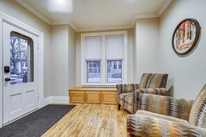 A room with a wooden floor, a bench, a patterned armchair, a door, and a window with blinds.