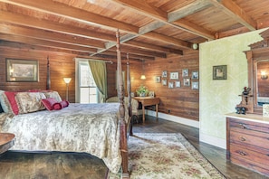 A wooden bedroom with a four-poster bed, a desk with a lamp, and a dresser.