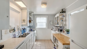 A compact kitchen with white cabinets, a wooden countertop, and a window with sheer curtains.