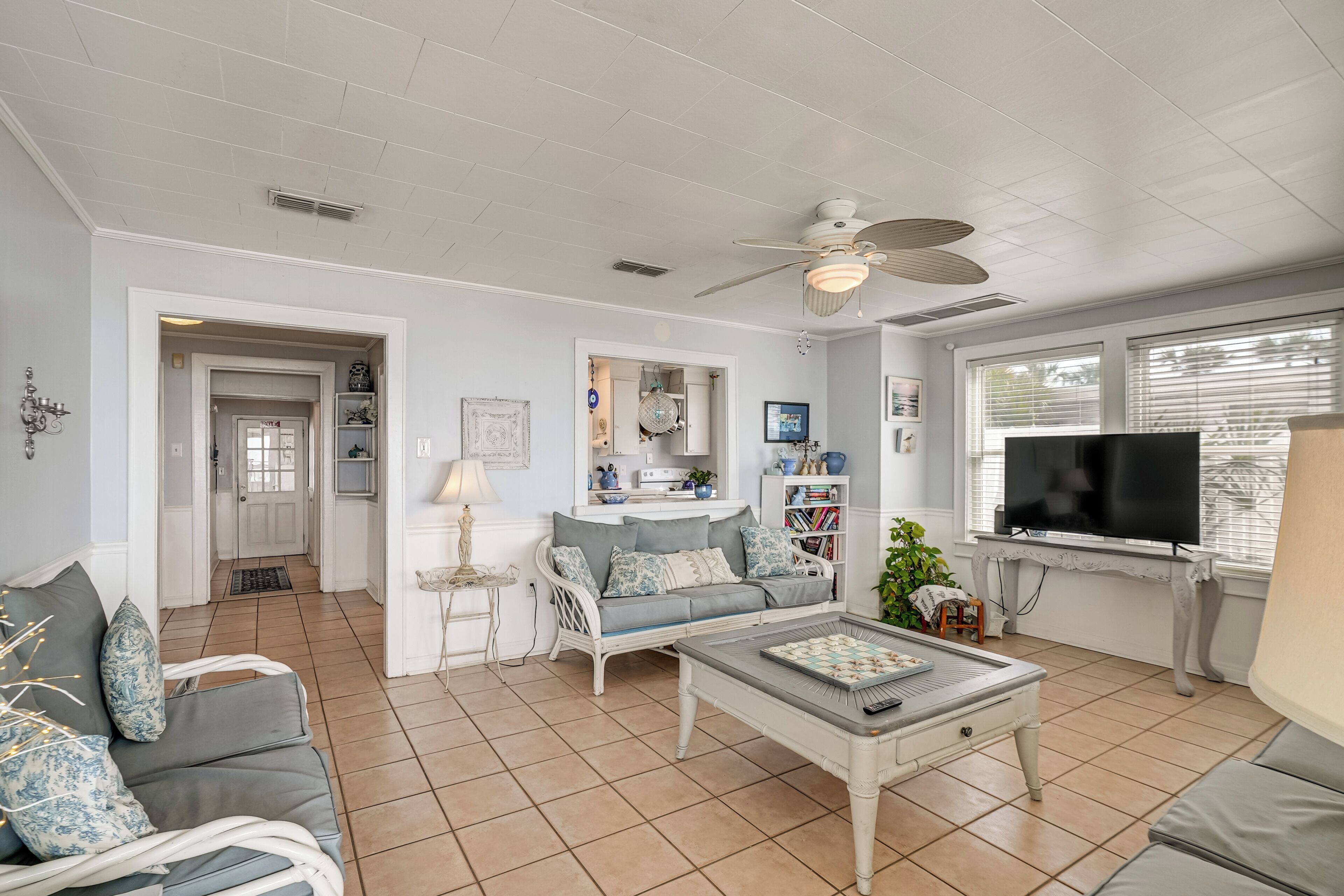 A living room with a white ceiling, a ceiling fan, a grey sofa, a coffee table, a television, and a bookshelf.