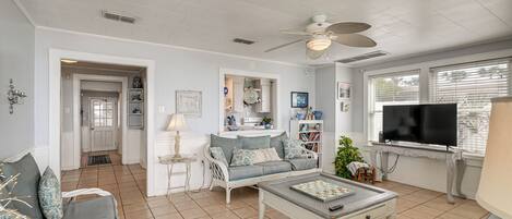 A living room with a white ceiling, a ceiling fan, a grey sofa, a coffee table, a television, and a bookshelf.