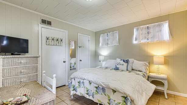 A bedroom with a bed, a television, a dresser, and a wicker chair.