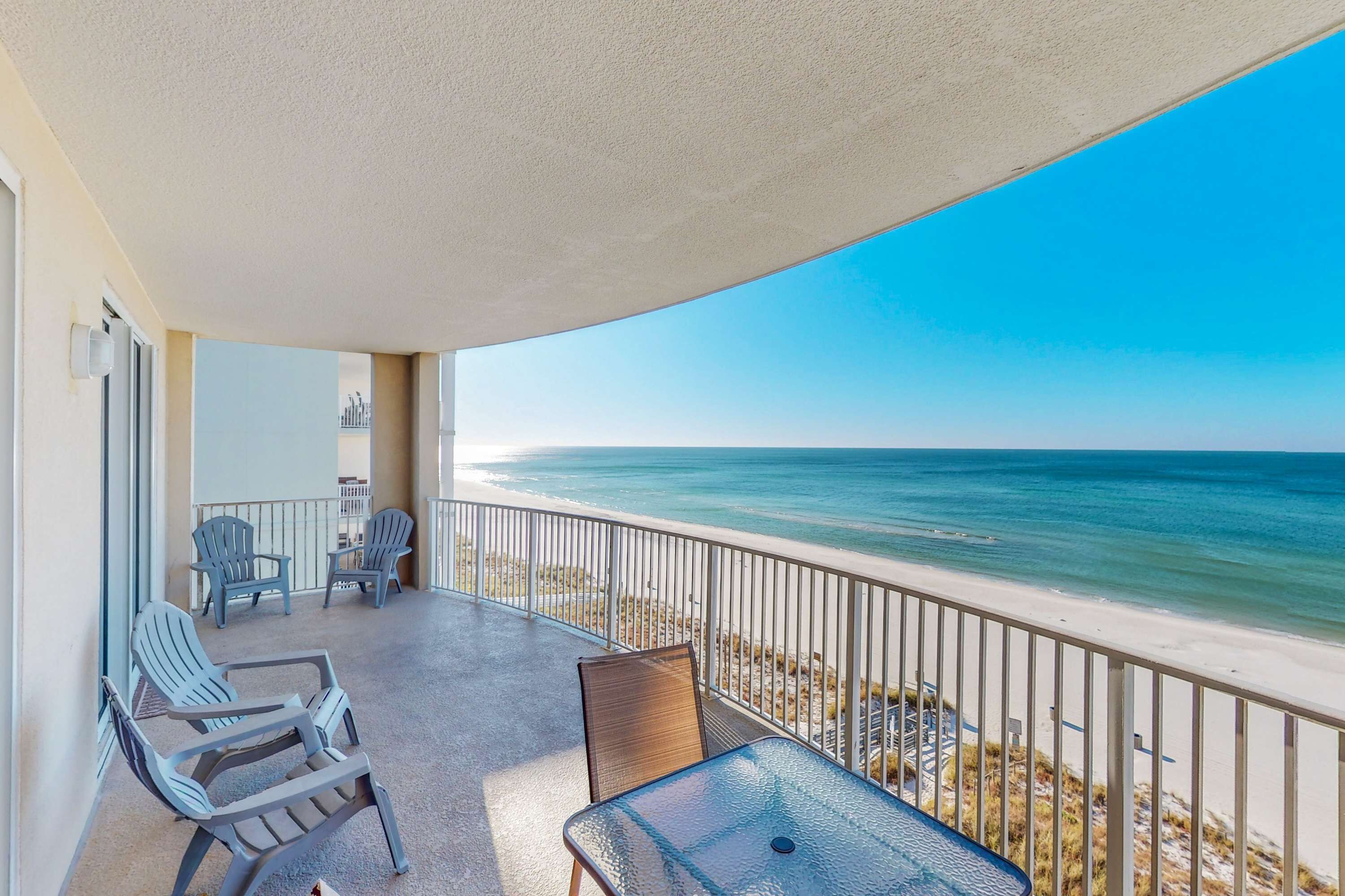 A balcony with a view of the ocean, a table, and two chairs.
