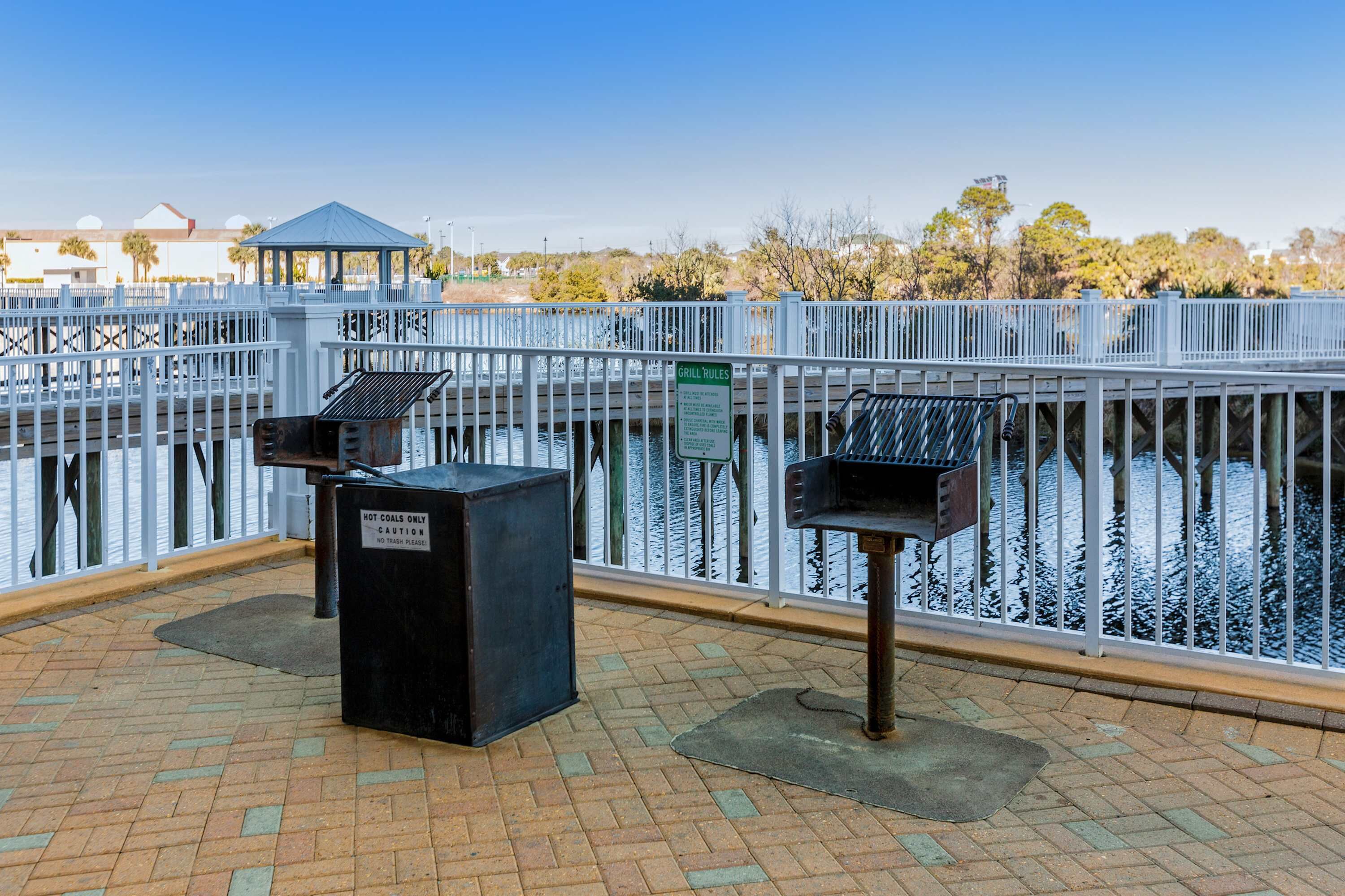 A covered outdoor area with a metal railing, a gazebo, and two grill stations.