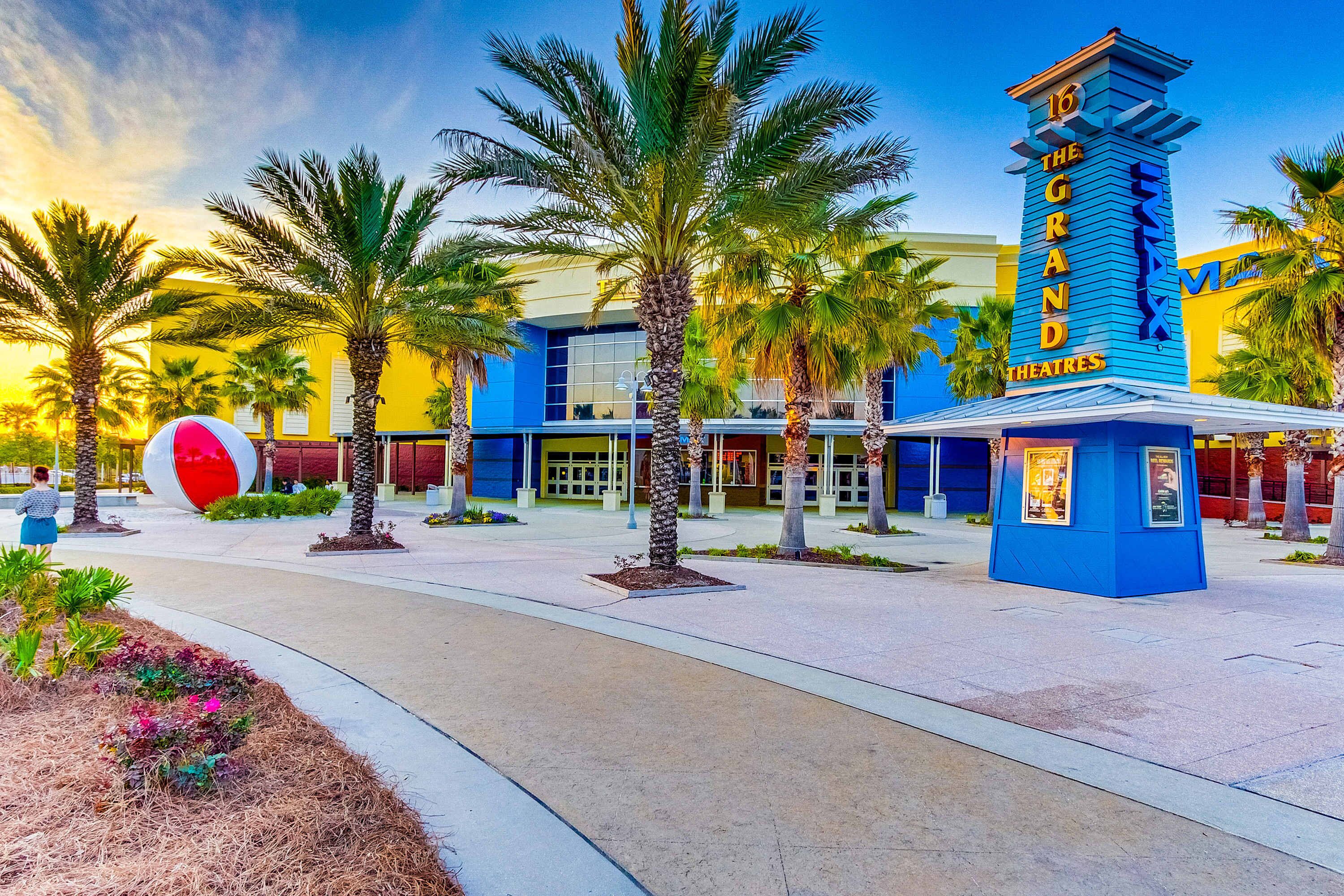 The Grand Theaters with a blue facade, palm trees, and a large red and white sculpture.