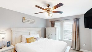 Un dormitorio con cama, mesitas de noche, ventilador de techo, armario y ventana con cortinas.