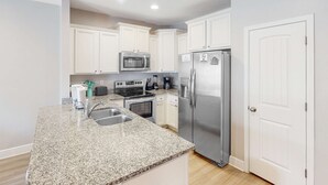 Una cocina moderna con armarios blancos, electrodomésticos de acero inoxidable, encimeras de granito y horno empotrado.