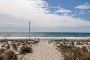 Ein Sandweg am Strand, der zum Meer führt, mit blauem Himmel.