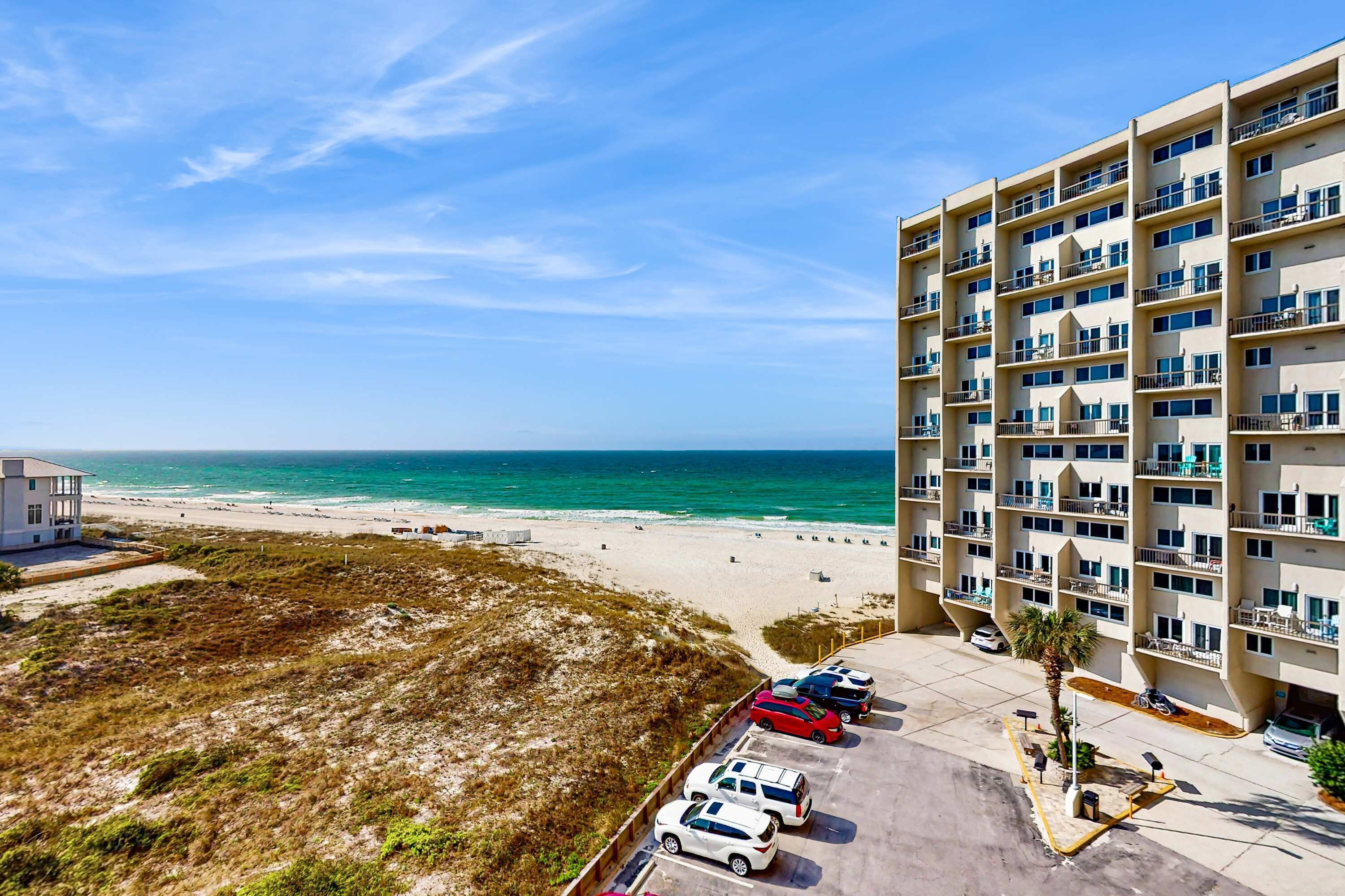 Ein Hotel direkt am Strand mit mehreren Balkonen, einem Parkplatz und Blick aufs Meer.