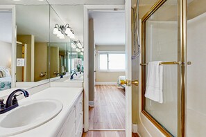 Un bany amb un mirall gran, un lavabo, una dutxa amb porta de vidre i una tovallola penjada a la porta.